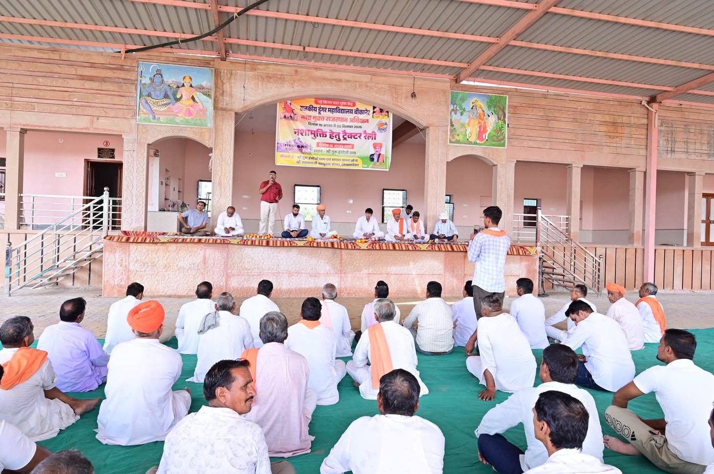 ग्राम सभा में मंच पर बैठे अतिथि और सामने ज़मीन पर बैठे ग्रामवासी